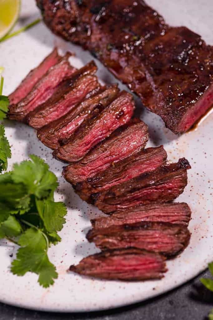 close up of sliced carne asada steak on white plate 
