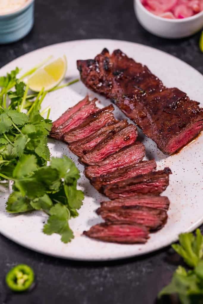 grilled carne asada skirt steak on a white plate with cilantro on a white plate