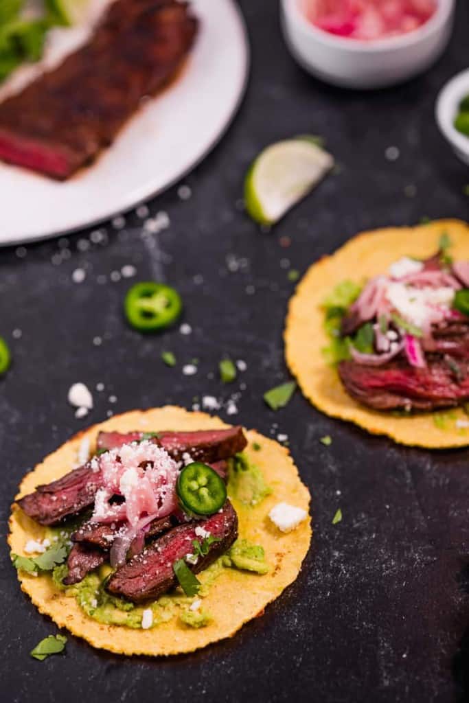 sliced skirt steak on a corn tortilla topped with cotija cheese and pickled red onions