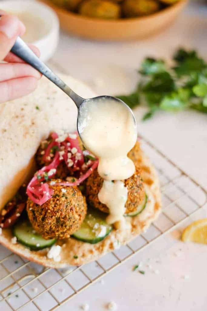 tahini sauce being drizzled over falafel