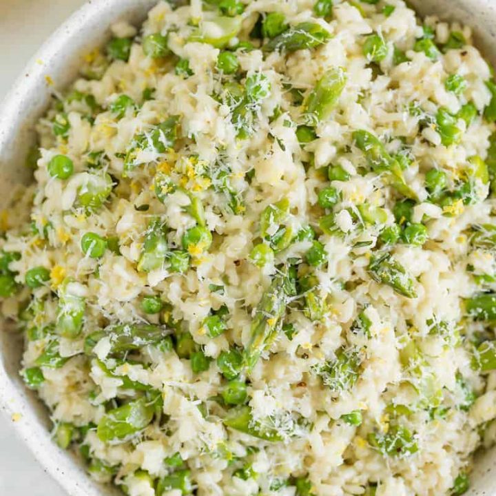 Risotto in a white bowl with asparagus, peas, and lemon zest on top