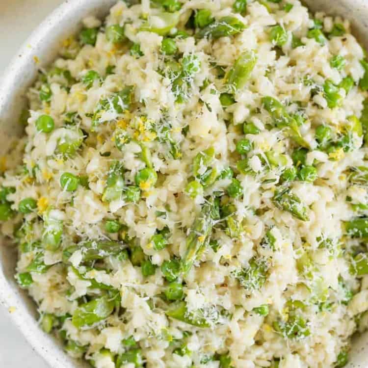 Risotto in a white bowl with asparagus, peas, and lemon zest on top