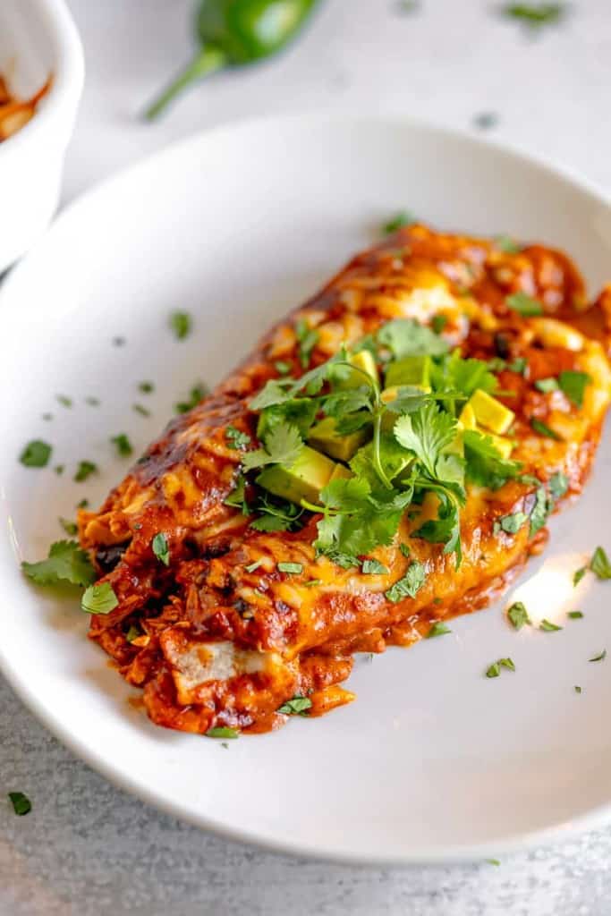 close up of two chicken enchiladas on a plate topped with cilantro and avocado
