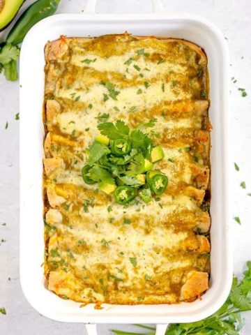 overhead of enchiladas verdes in a white baking dish topped with cilantro and avocado