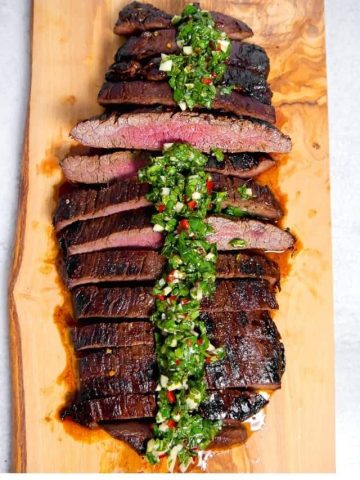 sliced grilled flank steak with chimichurri drizzled over the top