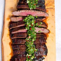 grilled flank steak sliced and topped with chimichurri over the top on a wooden block