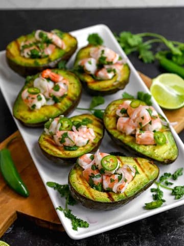 grilled avocado halves with shrimp ceviche and serrano peppers on a white plate