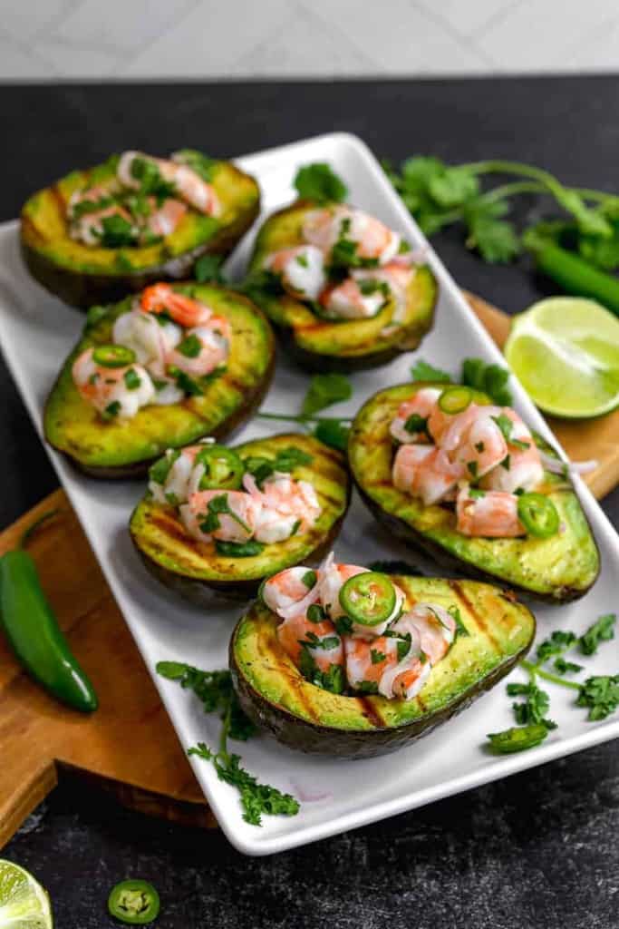 grilled avocado halves with shrimp ceviche and serrano peppers on a white plate