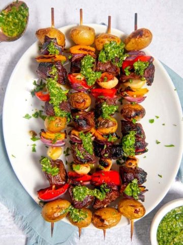 grilled steak and vegetable skewers with chimichurri sauce over top