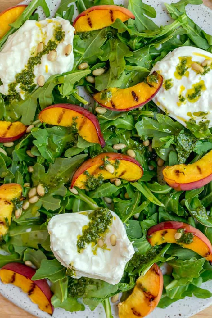 close up of bed of arugula with grilled peach slices, burrata, and basil dressing
