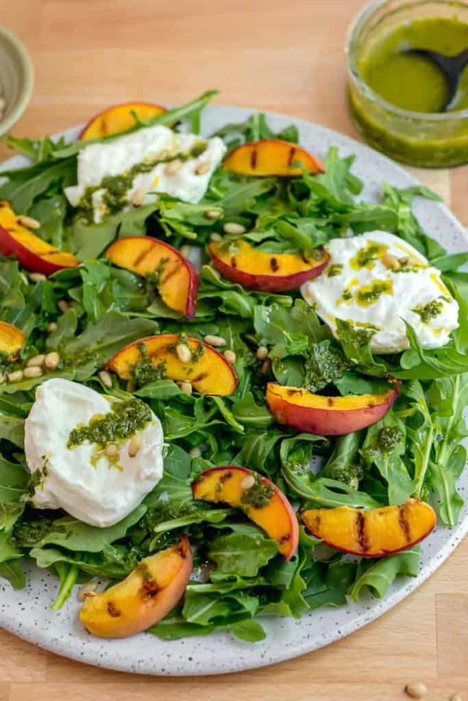 plate of arugula with sliced grilled peaches, torn burrata cheese, and basil oil over top