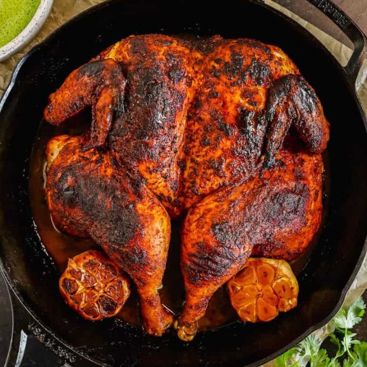 overhead shot of roasted peruvian spatchcocked chicken in a cast iron with roasted garlic