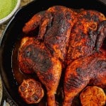Peruvian roasted spatchcock chicken in a cast iron skillet with aji verde green sauce and cilantro on the side