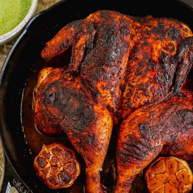 Peruvian roasted spatchcock chicken in a cast iron skillet with aji verde green sauce and cilantro on the side