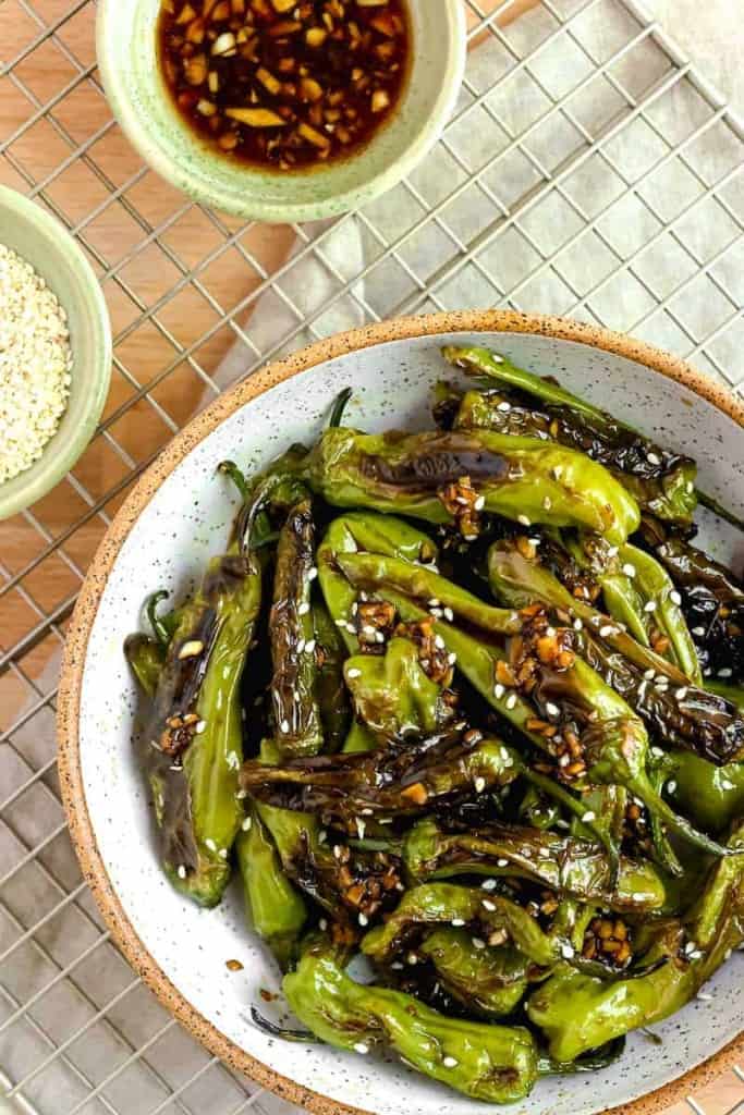 shishito peppers in a white bowl topped with soy garlic sauce and sesame seeds