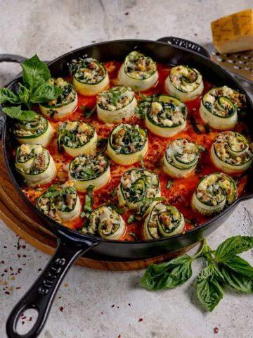 stuffed zucchini rolls in red sauce in a cast iron skillet topped with fresh basil