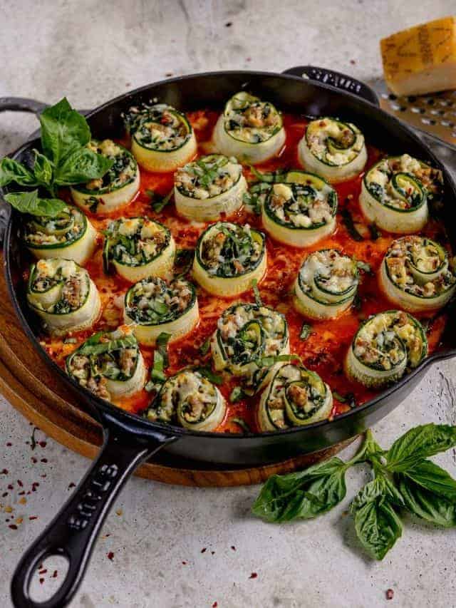 stuffed zucchini rolls in red sauce in a cast iron skillet topped with fresh basil