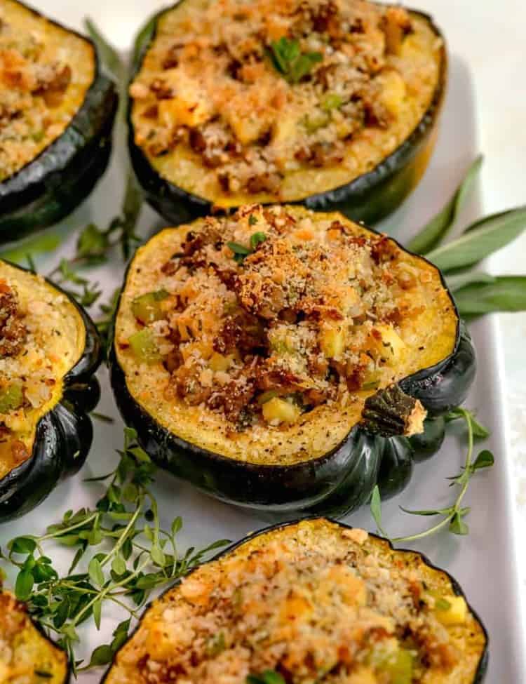 close up of stuffed acorn squash on a white platter surrounded by fresh sage
