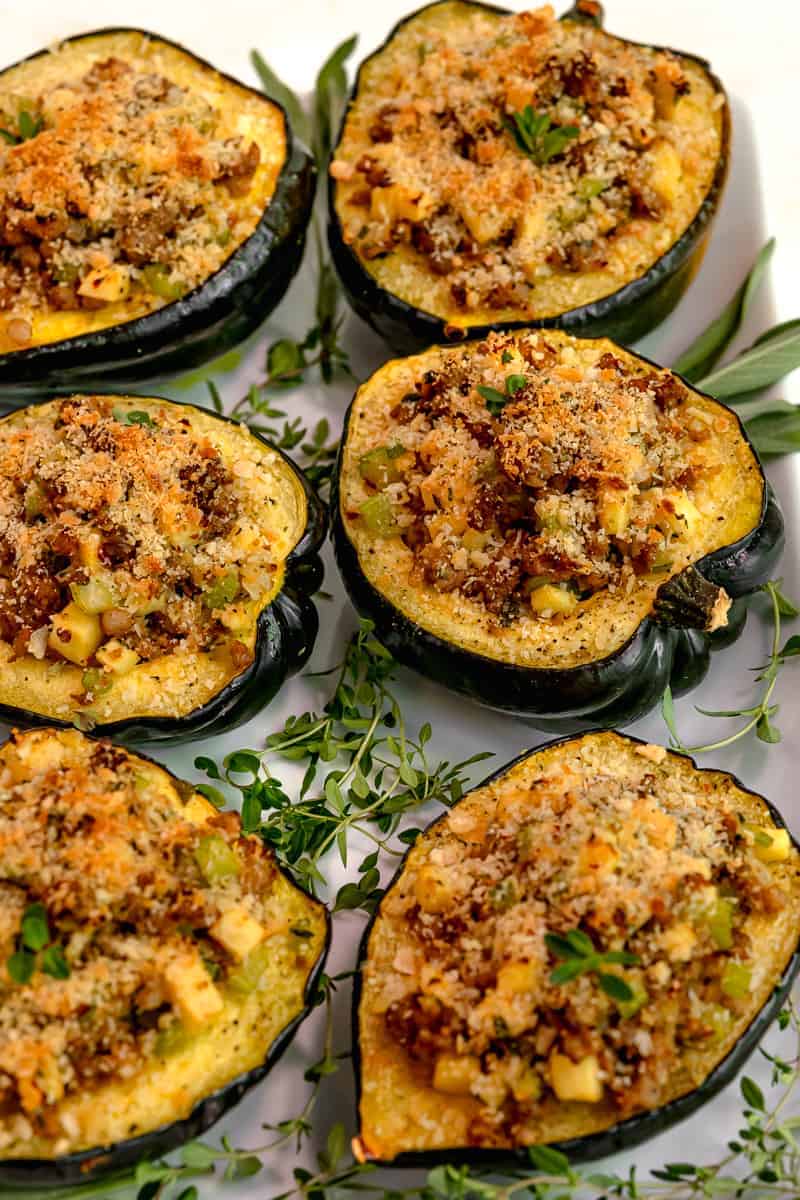 acorn squash cut in half and stuffed with italian sausage, apples, and topped with parmesan panko breadcrumbs. 6 stuffed squash on a white plate