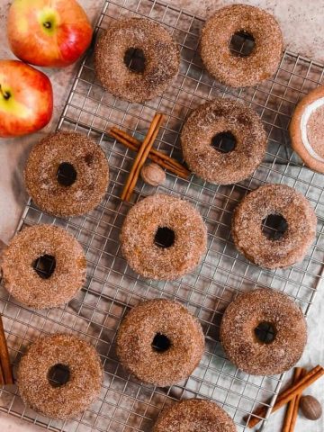 apple cider donuts coated in cinnamon sugar on a baking rack with cinnamon sticks
