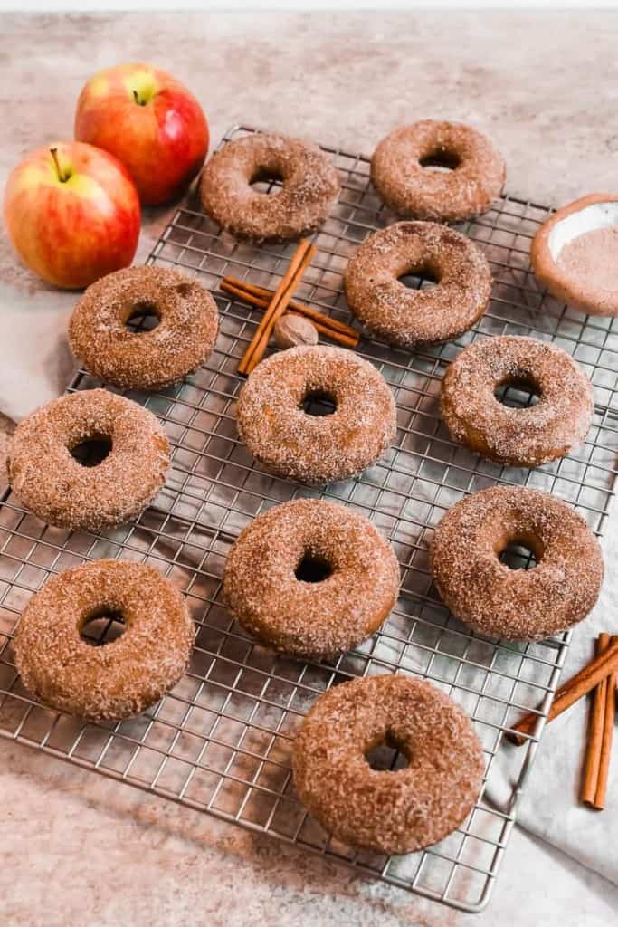 a dozen apple cider donuts coated in cinnamon sugar on a baking rack