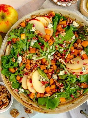 harvest salad in a bowl surrounded by an apple, walnuts, and pomegranate seeds