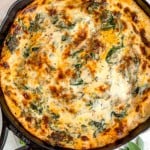 cast iron skillet with squash lasagna, melty cheese, and spinach on top surrounded by fresh thyme and sage