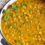 close up of pumpkin chickpea curry in a skillet with fresh cilantro garnished on top and basmati rice in a bowl in the background