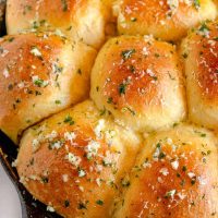 close up on minced garlic and parsley on top of dinner rolls