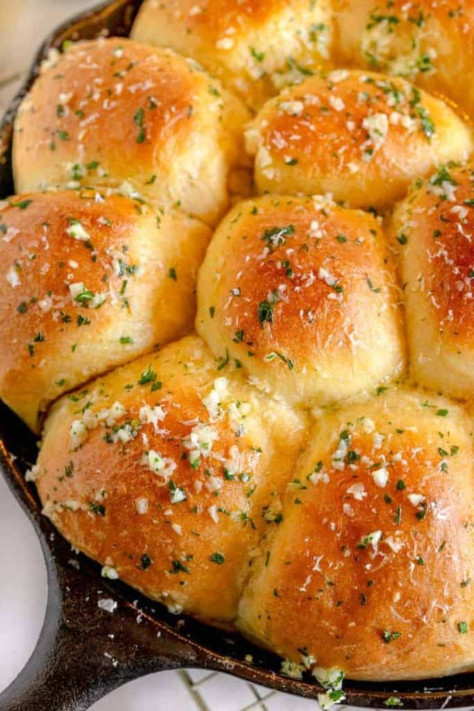 close up on minced garlic and parsley on top of dinner rolls 