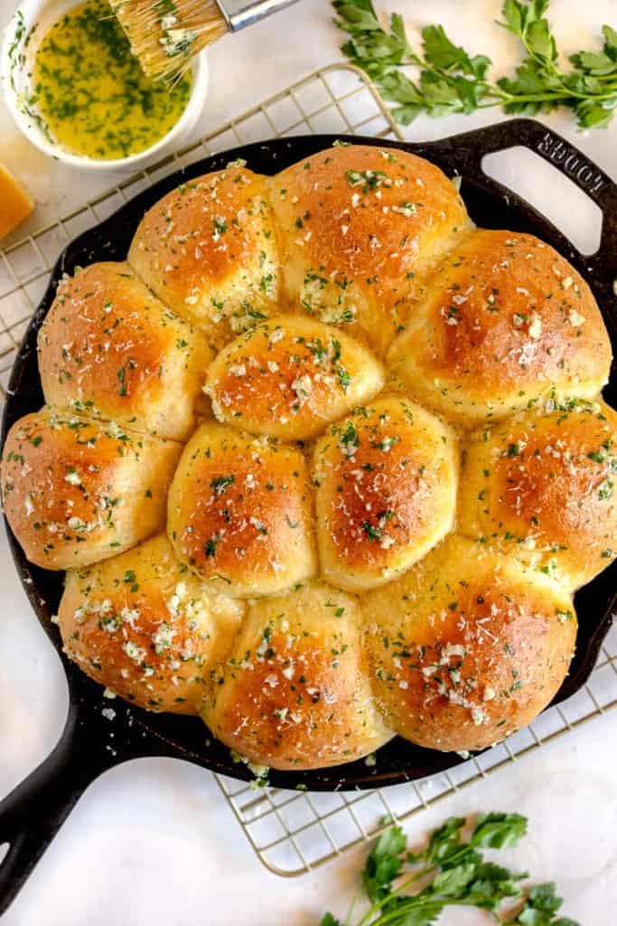 Cast iron skillet with garlic butter dinner rolls surrounded by fresh parsley