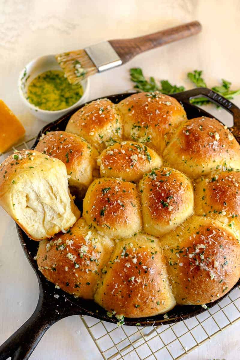 cast iron skillet with garlic butter dinner rolls and one dinner roll coming out of the pan