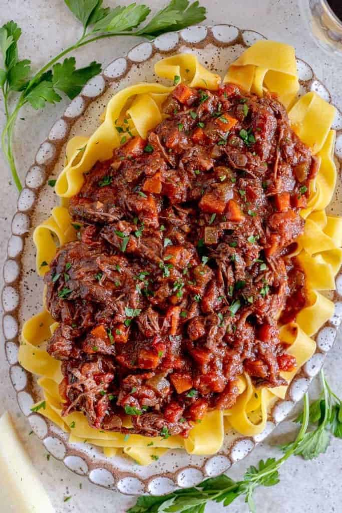 Plate of pappardelle pasta with shredded short rib ragu and parsley around plate