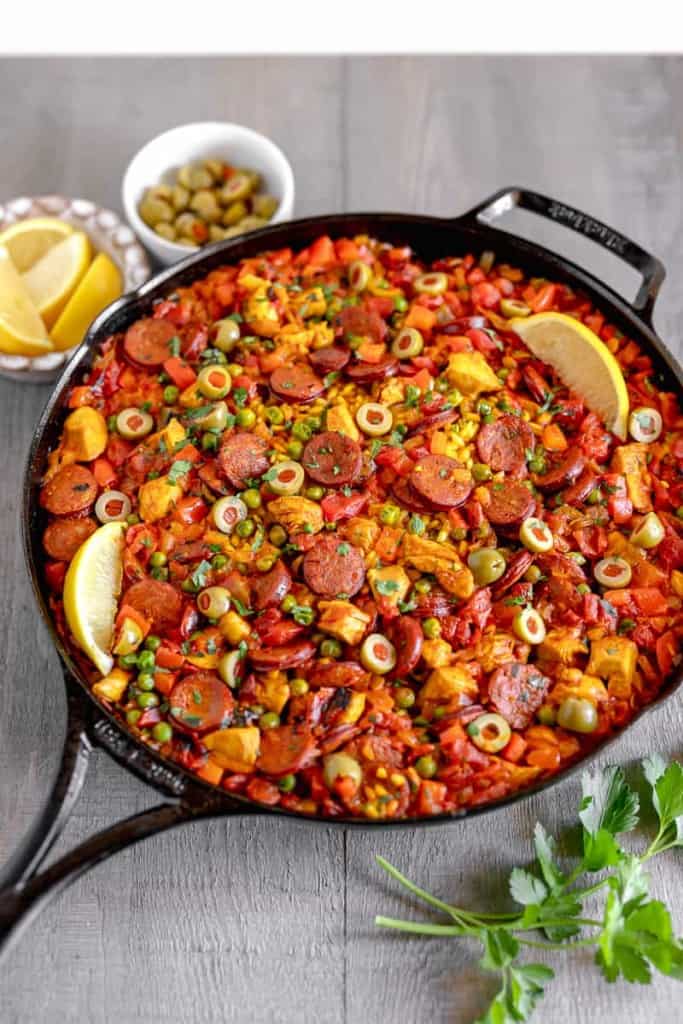 paella in a cast iron skillet with lemon wedges, olives, and fresh parsley surrounding the skillet