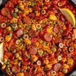 close up of chicken and chorizo paella in a cast iron skillet topped with a lemon wedge