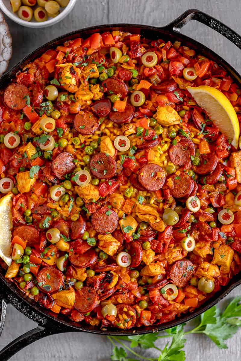 close up of chicken and chorizo paella in a cast iron skillet topped with a lemon wedge