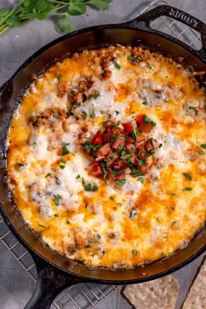 queso fundido with chorizo in a cast iron skillet topped with diced tomatoes and cilantro