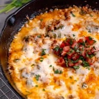 queso fundido in a cast iron skillet topped with diced tomatoes