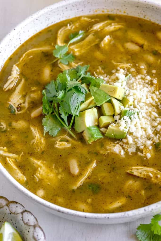 close up of roasted tomatillo chicken soup topped with cotija cheese, avocado, and fresh diced avocado