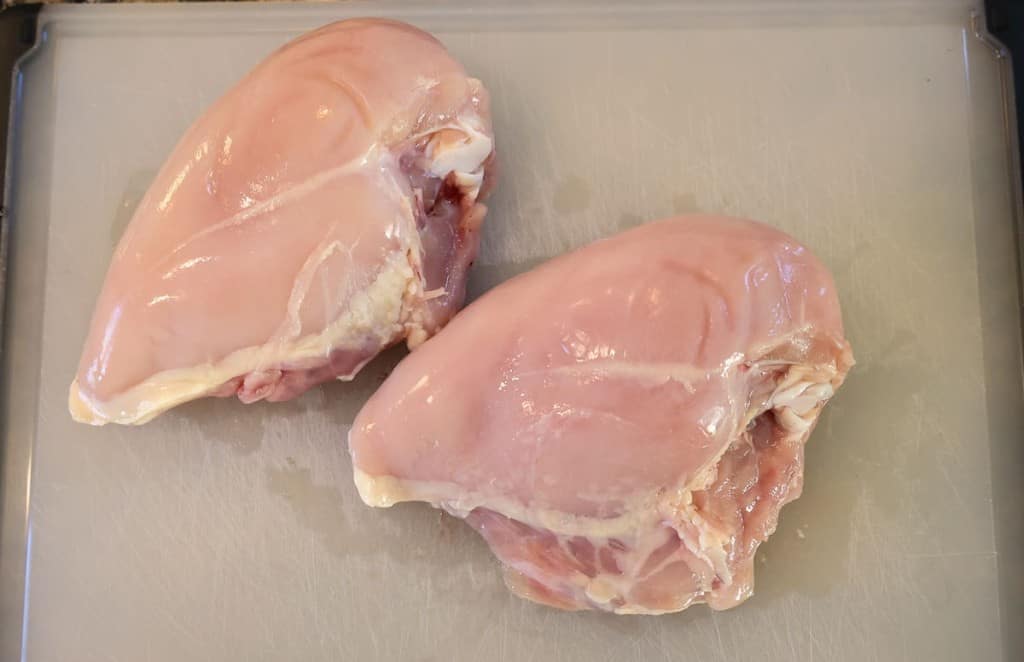 bone-in raw chicken breast on a white cutting board