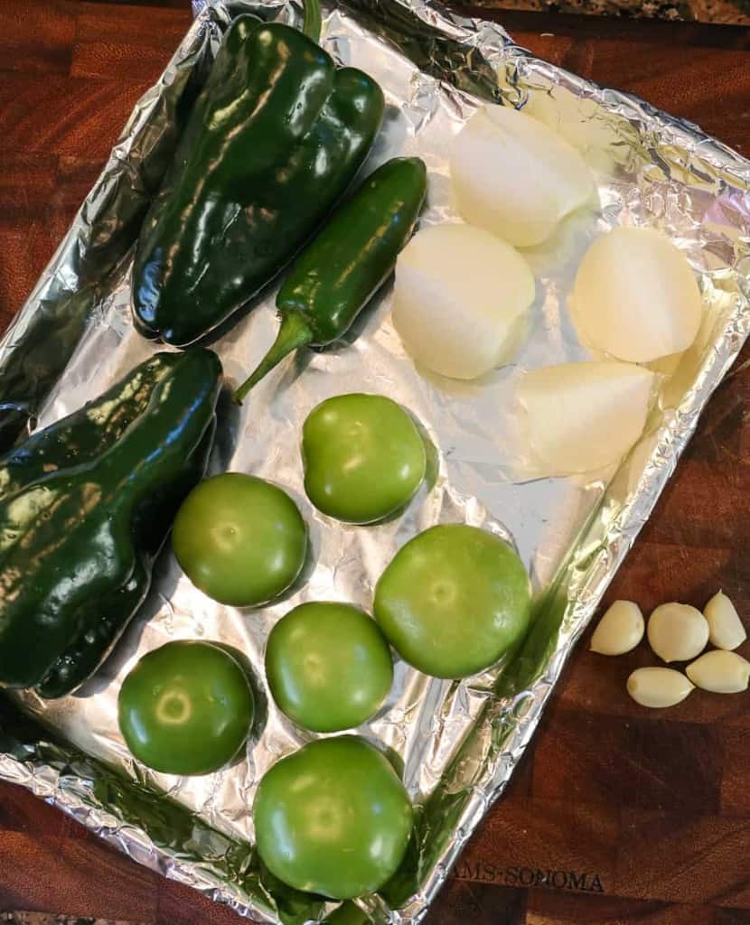 whole poblano peppers, jalapenos, tomatillos, onion, and garlic on a sheet pan