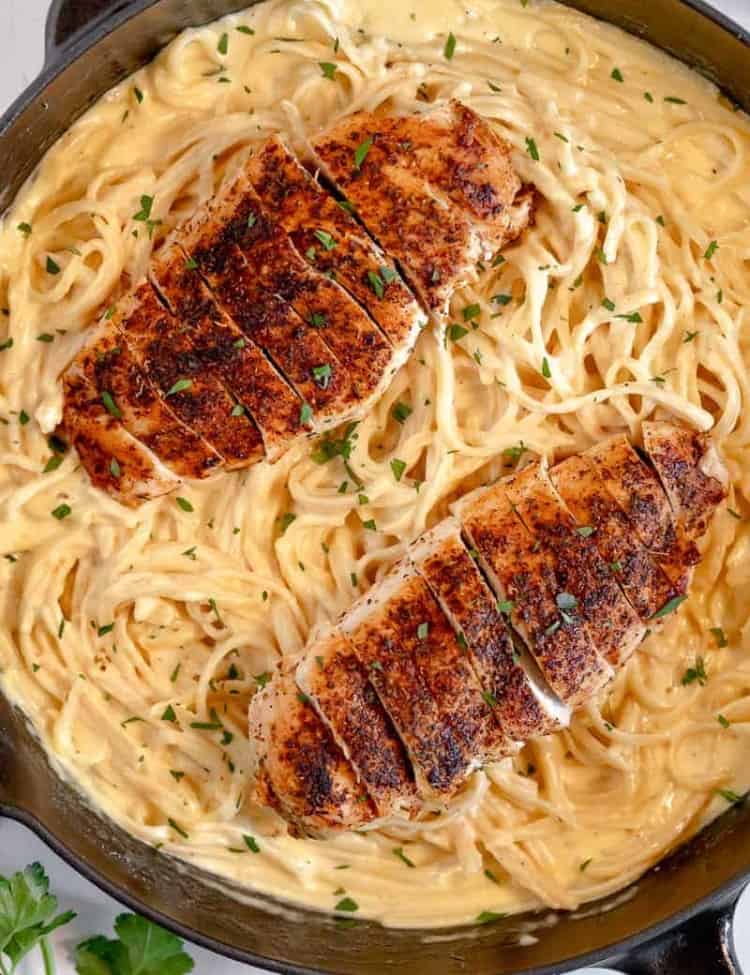 cast iron skillet on white background filled with creamy Alfredo pasta and sliced blacked chicken breast on top of pasta