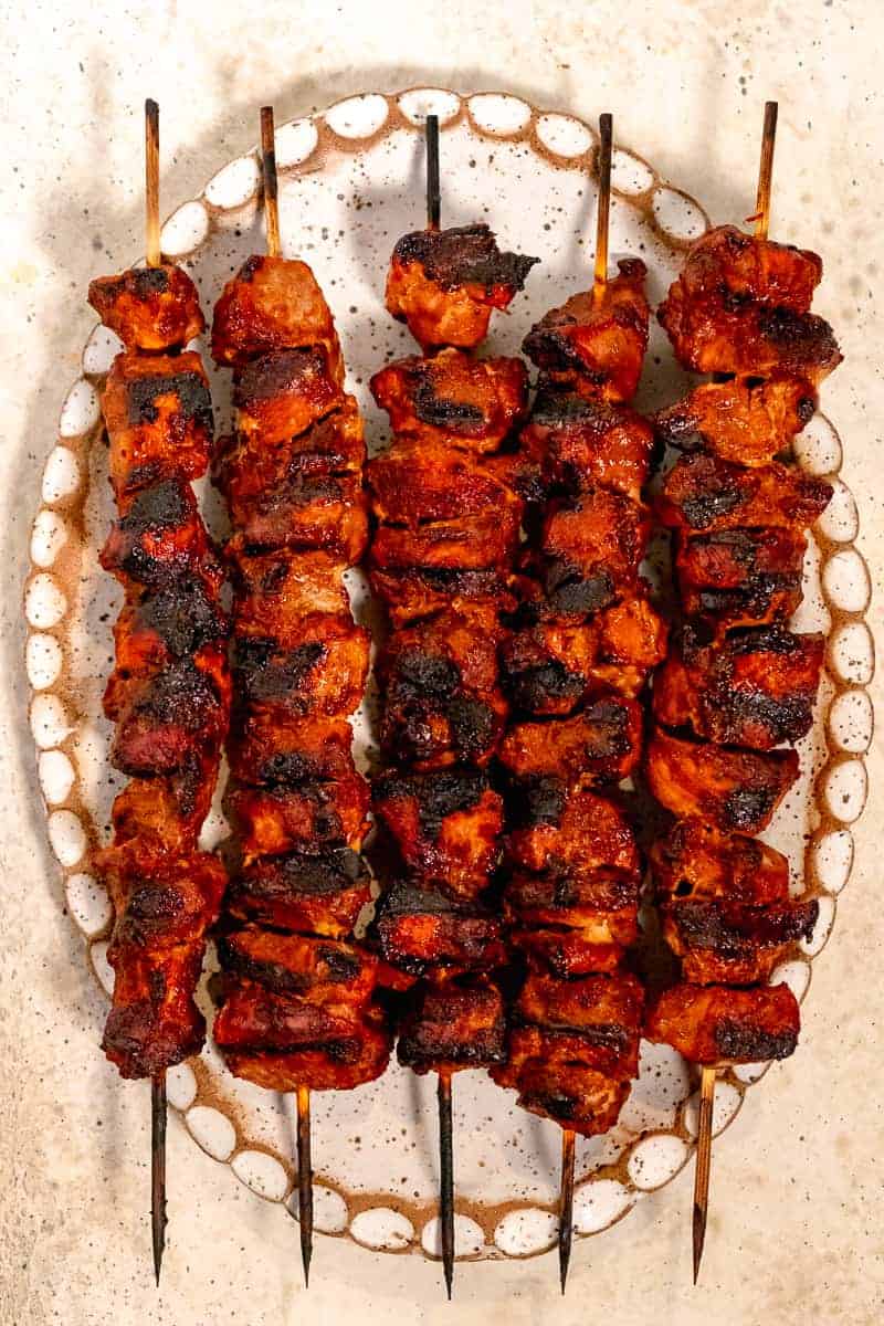 skewered pork al pastor on wooden skewers with char marks from grill on a white oval plate