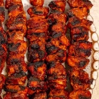 skewered pork al pastor on wooden skewers with char marks from grill on a white oval plate