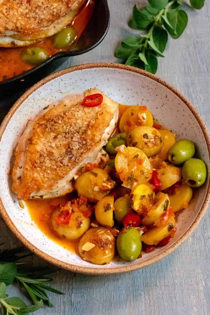 bowl of chicken with potatoes, olives, peppers, and juice at bottom of white bowl