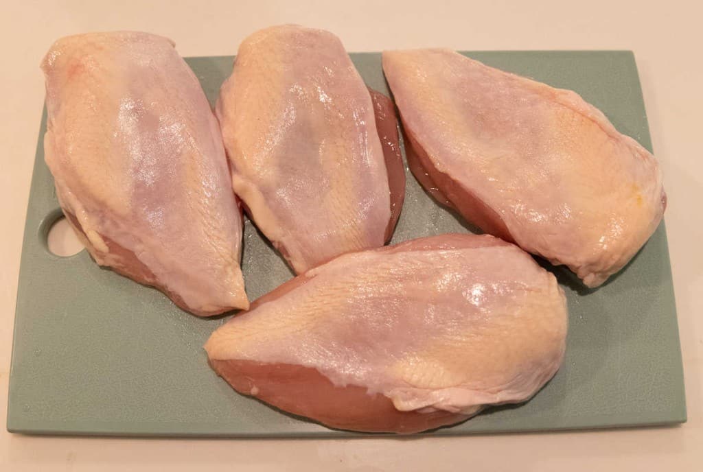 raw skin on chicken breast on a green cutting board