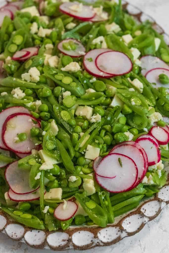 close up photo of sliced snap peas on a white and brown speckled plate with thinly sliced radishes