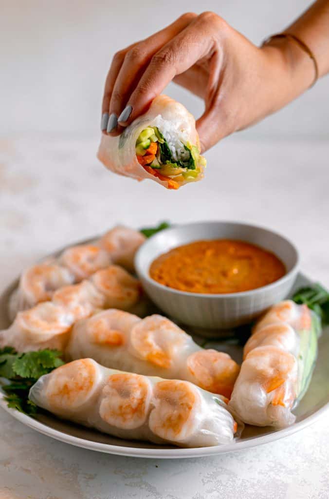 A shrimp spring roll with a bite taken out of it showing a rainbow of vegetables inside