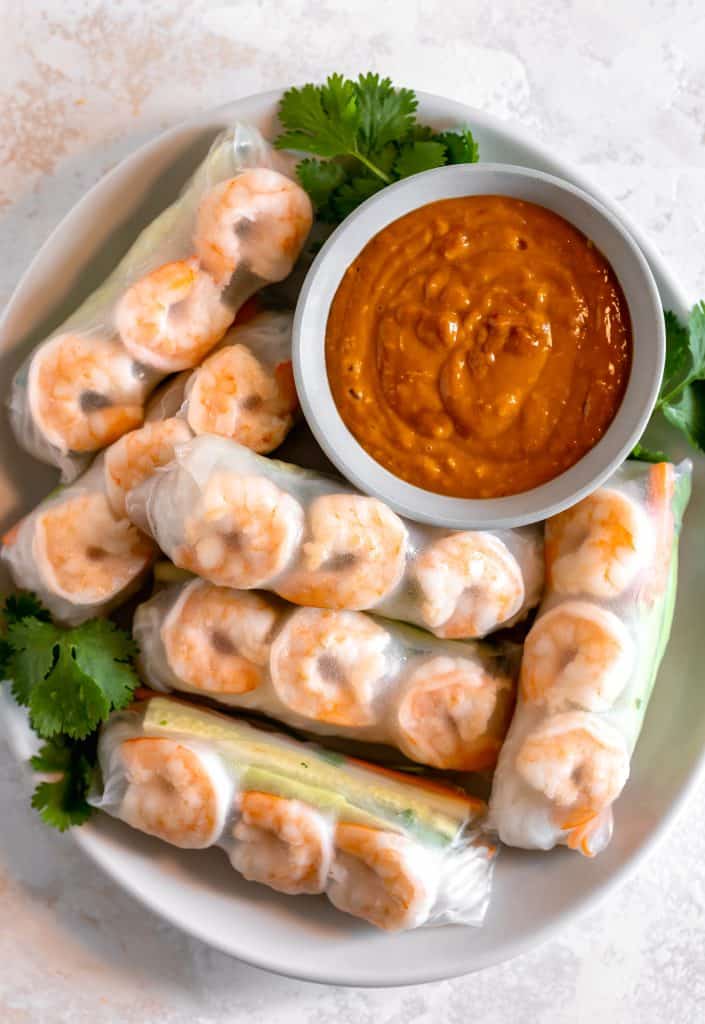 a plate of spring rolls wrapped in rice paper with a bowl of spicy peanut sauce in top right corner