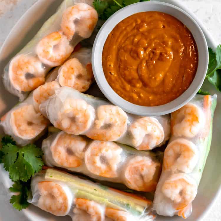 a plate of spring rolls wrapped in rice paper with a bowl of spicy peanut sauce in top right corner
